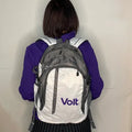 Person mit schulterlangem braunem Haar, von hinten zu sehen, trägt eine lila Jacke und einen grauen Rucksack mit weißen Flächen. Auf dem Rucksack steht in lila Schrift 'Volt'.
